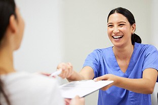 Dental assistant smiling while handing patient form