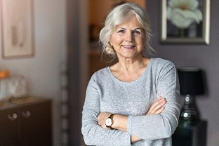 Senior woman in grey shirt smiling with arms folded