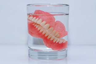 Dentures soaking in glass of liquid