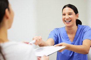 Dental assistant smiling while handing patient form