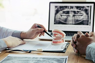 Nose-to-shoulder view of woman with white hair smiling and touching cheeks
Two pairs of hands at desk going over X-rays, toy teeth, and other paperwork