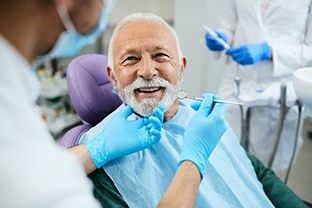 Man with white hair in dental chair smiling before having teeth examined